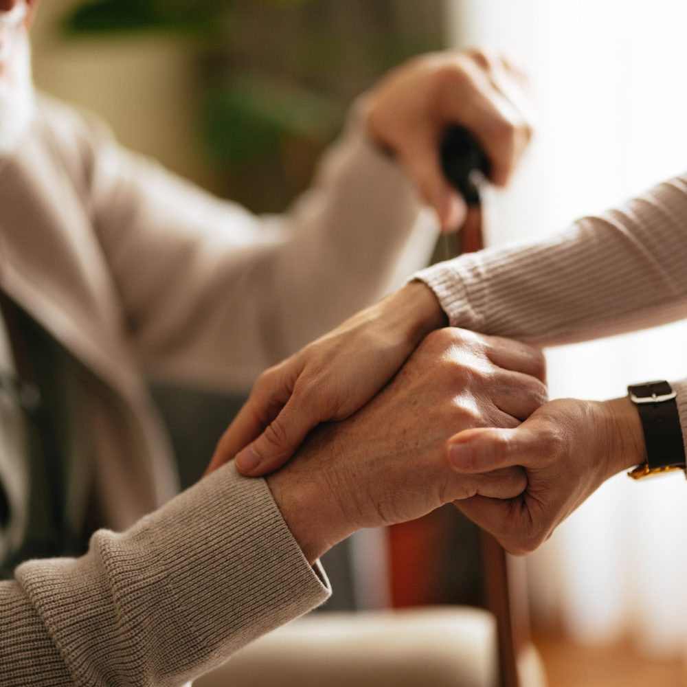 Unrecognizable Japanese female caregiver supporting her smiling elderly patient to stand up.
